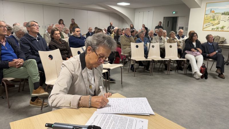 Caroline de Raimond écrit à une table, micro posé devant elle, face aux paroissiens assis qui écoutent.